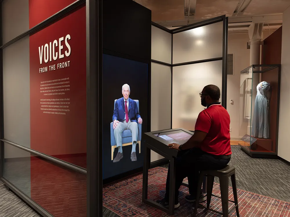 A visitor sits across from a video of a veteran on a screen