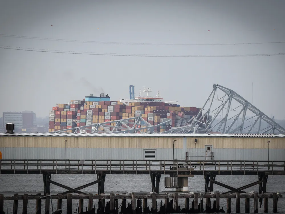 a large container ship in a river with ruins of a truss bridge on top of it