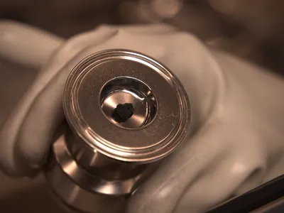 A tiny black rock from an asteroid sits in a metal container