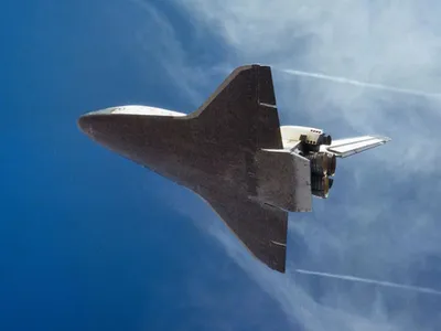 Underside view of space shuttle in flight with blue sky background.