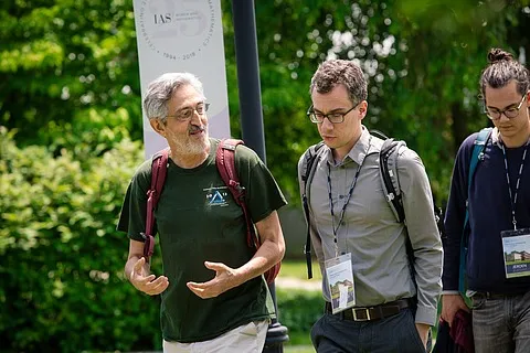 Avi Wigderson (left), walks next to two other men on a path outside